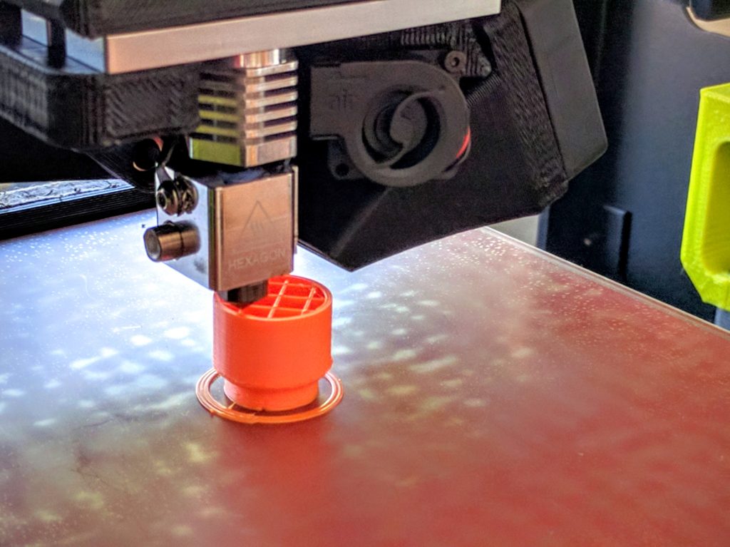 Printing a (different) part. Solid shapes are generally filled with an infill pattern, here the visible cross-grid, to maintain strength and form while dramatically reducing material and print time.